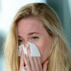 Blondynka z piegami chusteczką wyciera nos. Może to być objaw przeziębienia, alergii lub po prostu emocji. Jovesto.