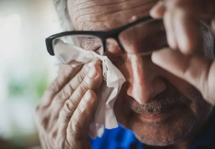 Starszy mężczyzna w okularach wyciera łzę chusteczką. Może to być objaw smutku lub reakcja alergiczna, np. na peritol.