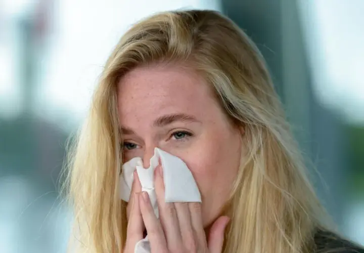 Blondynka z piegami chusteczką wyciera nos. Może to być objaw przeziębienia, alergii lub po prostu emocji. Jovesto.