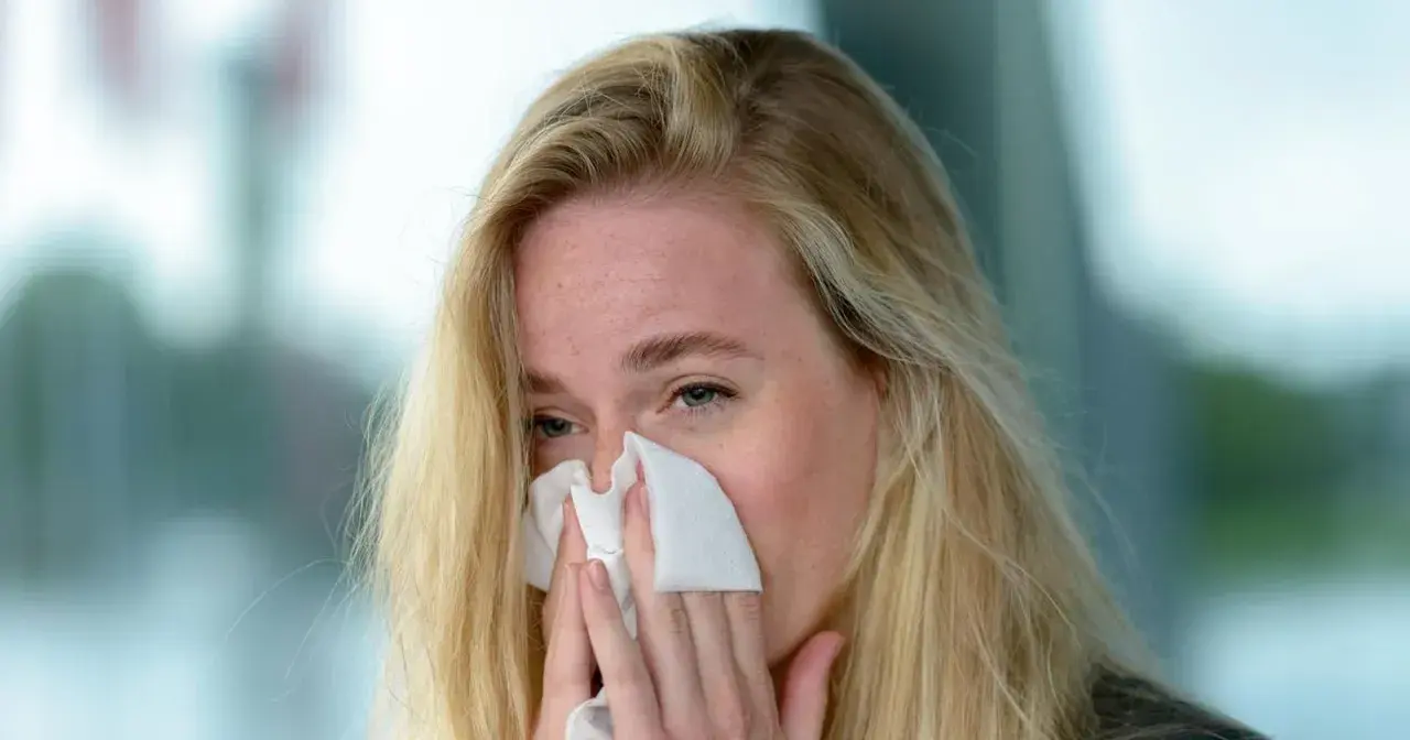 Blondynka z piegami chusteczką wyciera nos. Może to być objaw przeziębienia, alergii lub po prostu emocji. Jovesto.