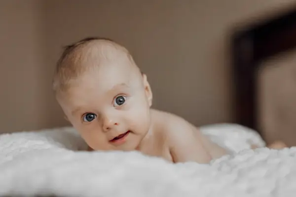 Niemowlę na brzuchu, z zaciekawieniem patrzące w obiektyw. Jego oczy, choć mogą sugerować zez u niemowlaka, są po prostu skupione na otoczeniu.